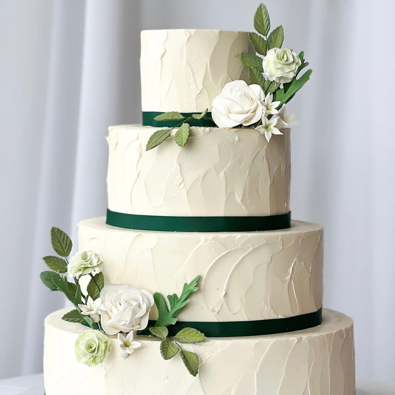 Three-tiered wedding cake with white flowers and green ribbons on a white background Seattle wedding